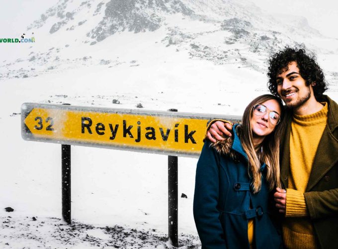 A joyous couple stands in front of the Reykjavik sign board, surrounded by a winter wonderland of glistening snow.