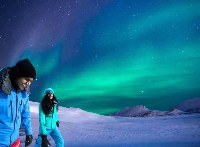 Indian couple delightedly watching the Northern Lights in Finnish Lapland during their 7 nights 8 days Northern Lights tour package.