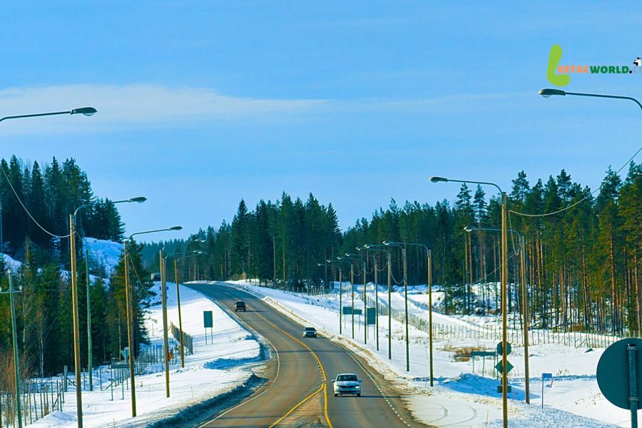 A scenic road in Swedish Lapland surrounded by snow-covered trees, with a cab traveling from Kiruna to Rovaniemi under a clear blue sky.