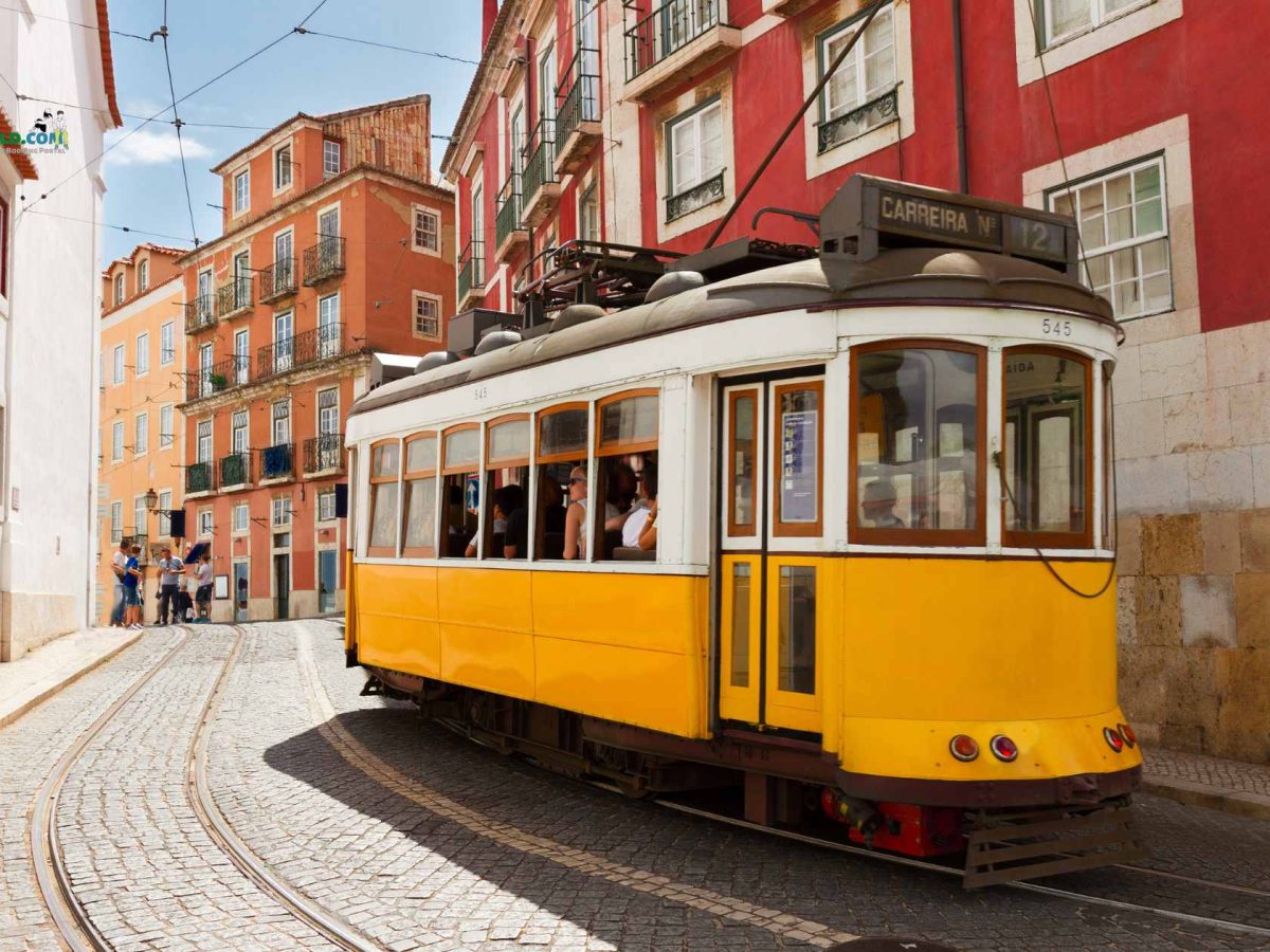A classic yellow tram passing through the historic streets of Lisbon, Portugal, with colorful buildings and cobblestone roads in the background.